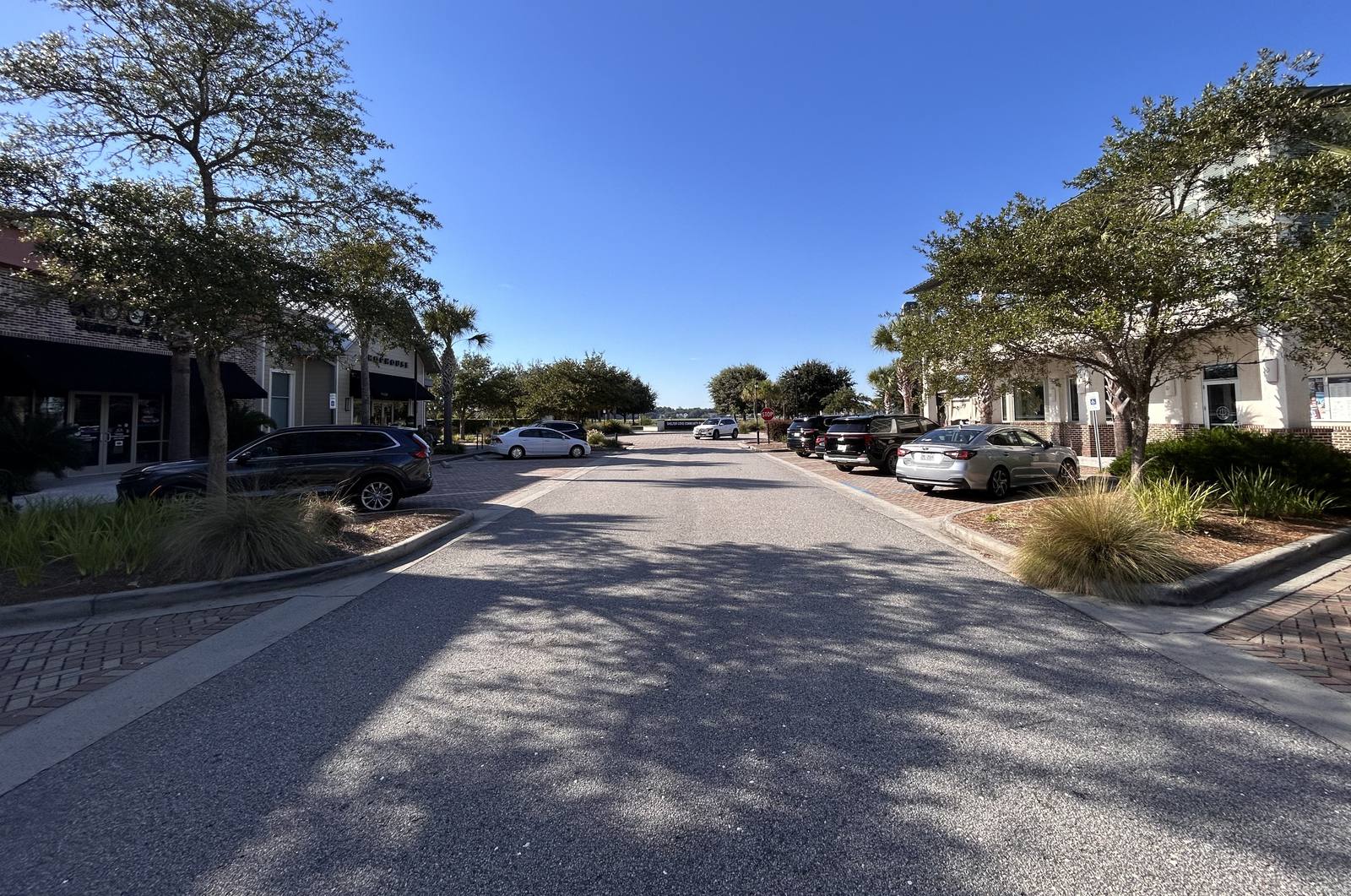 A Hilton Head street lined with storefronts and live oaks, opening onto Shelter Cove in the distance